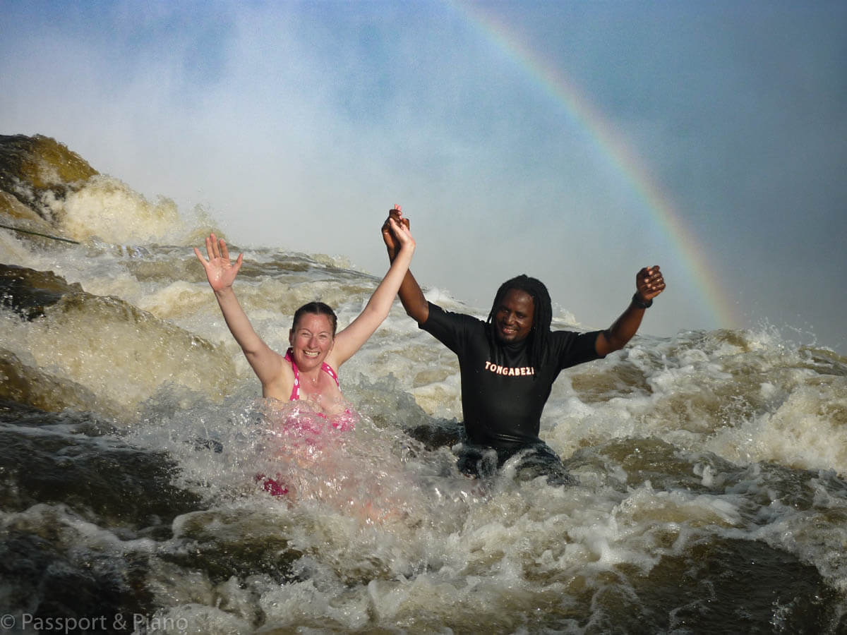 An image of me and the guide from Tongabezi with our arms in the air and a rainbow in the background.