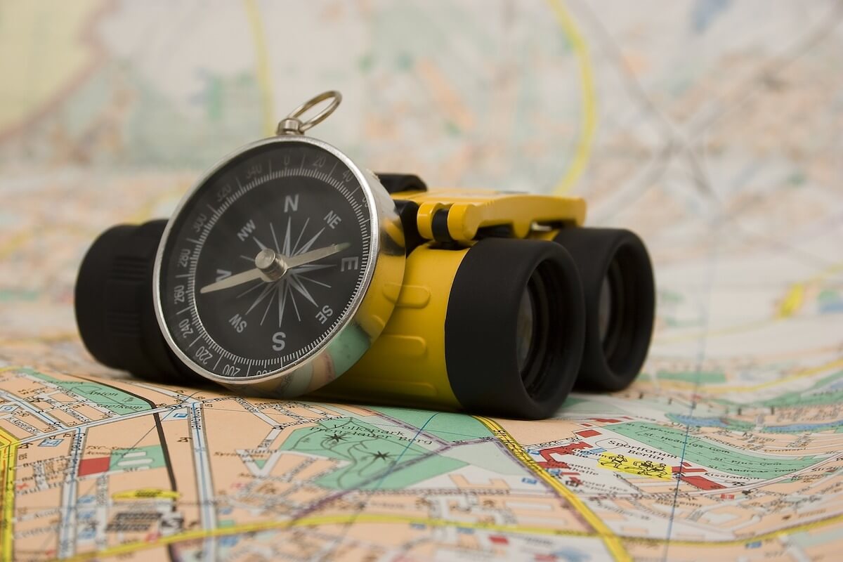 An image of a compass and a pair of yellow compact binoculars on a map