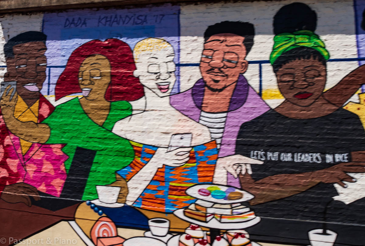 An image of a street art mural that has 5 people from different races sharing cake.
