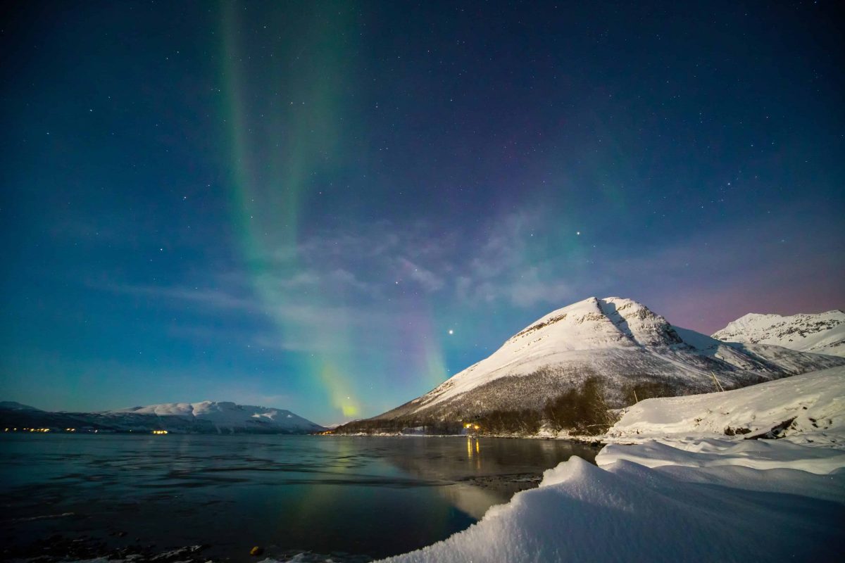 An image of the northern lights with snow capped mountains in the foreground