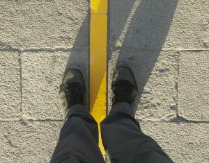 An image of a pair of black hiking boots with one foot on either side of a yellow line